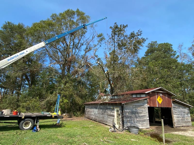 Crane boom extended over the damaged barn in Beulaville, NC, with the crane truck set up on the grass alongside.