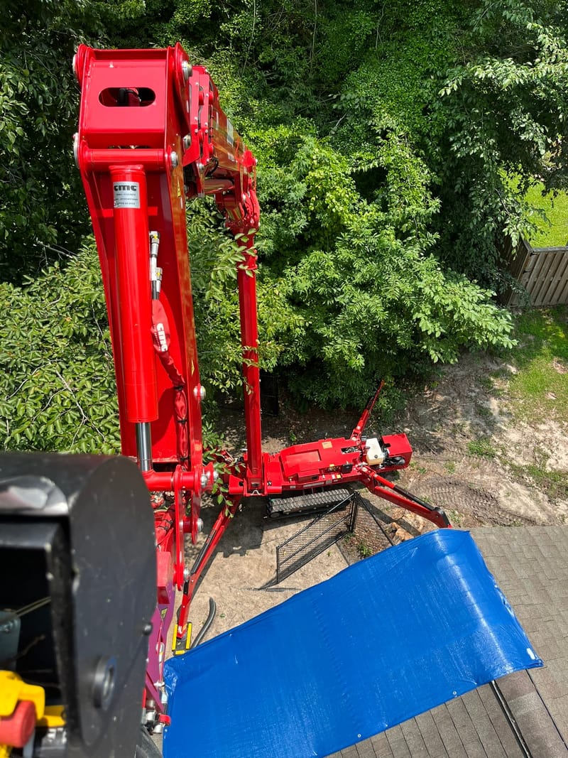 Looking down the lift boom to a blue tarp covering the damaged section of roof below.