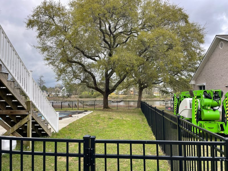 The lift set up behind a metal fence beside a large oak, with water behind the property.